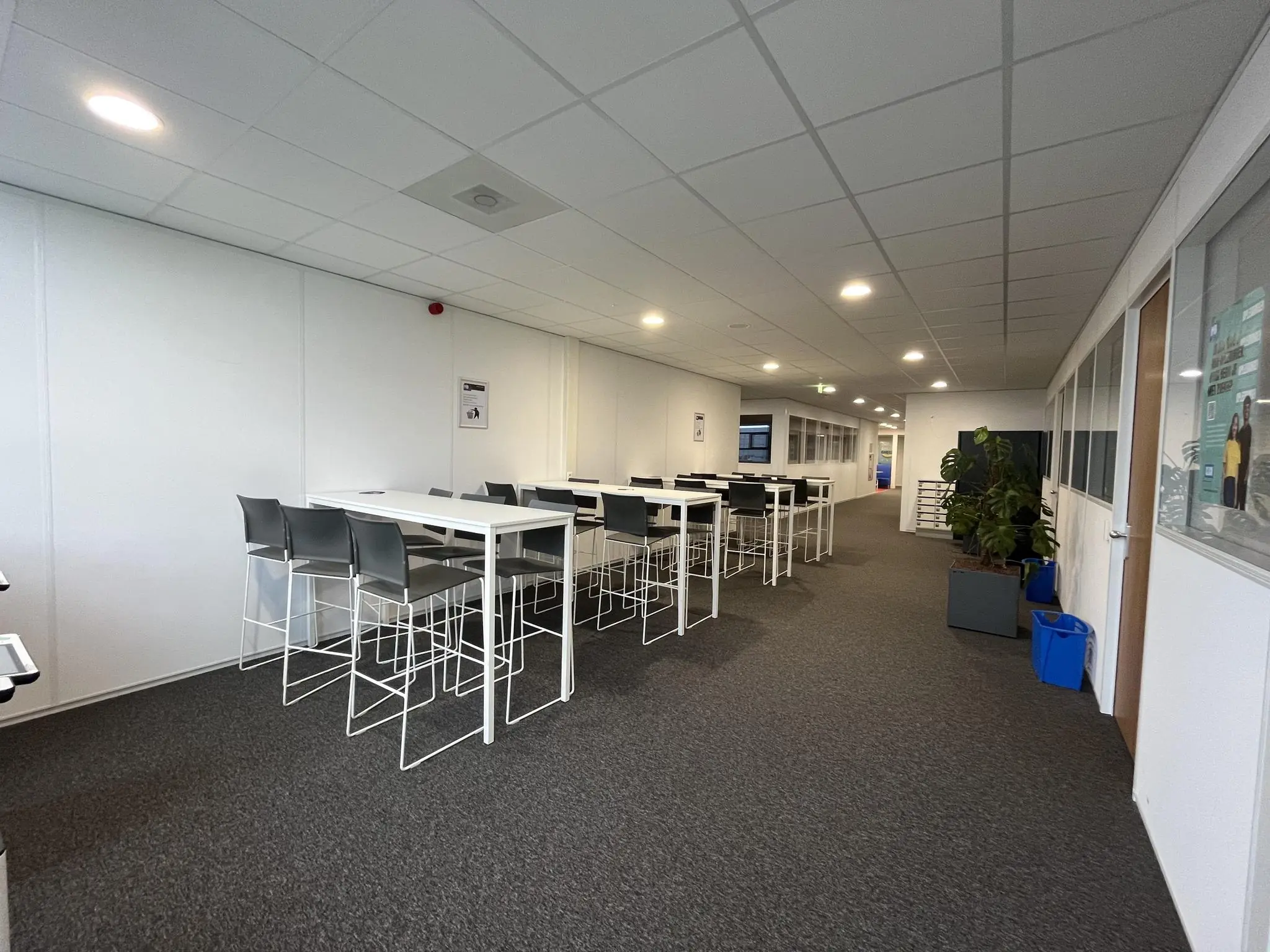 Moderne kantoorgang aan de Niels Bohrweg met hoge tafels, stoelen en planten.